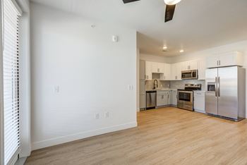 an empty living room with a kitchen with stainless steel appliances